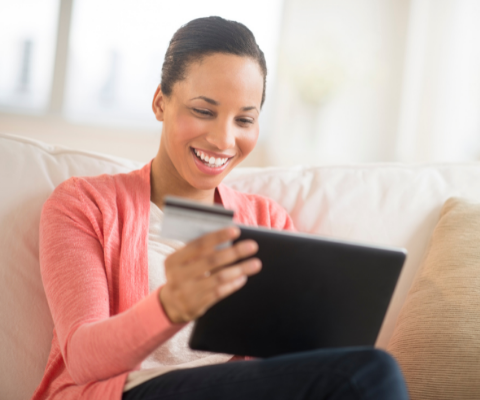 Smiling woman sitting on couch with a computer tablet on her lap and a credit card in her hand.