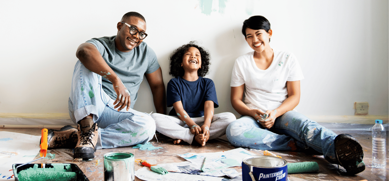 Family of three sitting on the floor with paint cans.