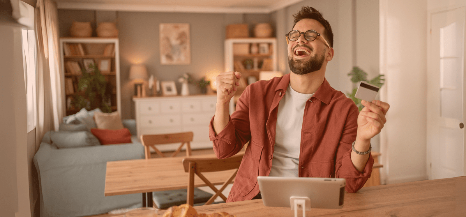 Smiling man holding a Debit Card and using a computer tablet.